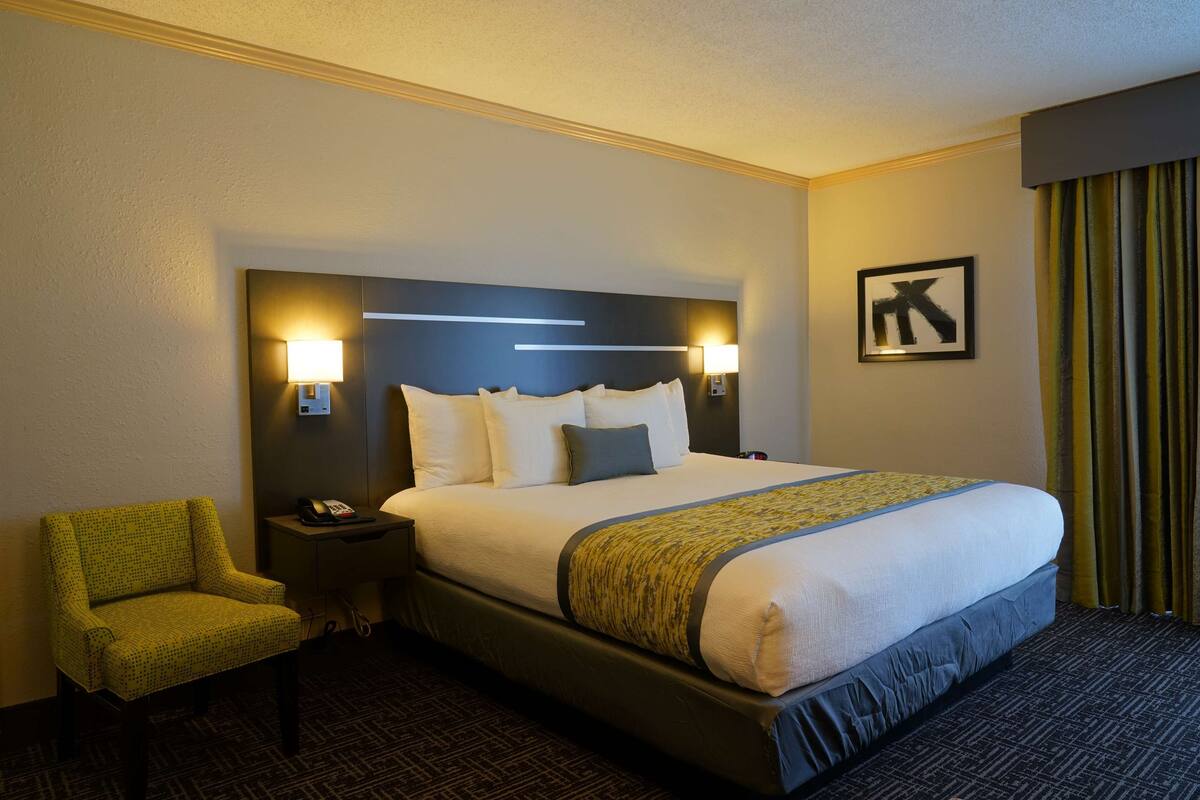 A hotel room with a large bed, two bedside lamps, a chair, and a framed picture on the wall.