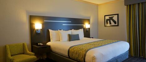 A hotel room with a large bed, two bedside lamps, a chair, and a framed picture on the wall.
