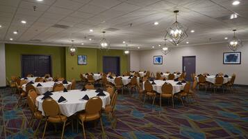 A conference room with multiple tables and chairs, arranged in rows, with ceiling lights and wall-mounted artwork.