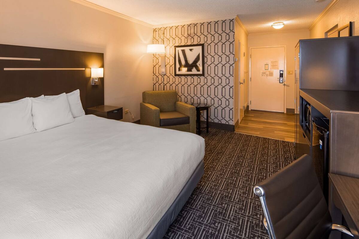 A hotel room with a large bed, a desk, a chair, a lamp, and a picture on the wall.