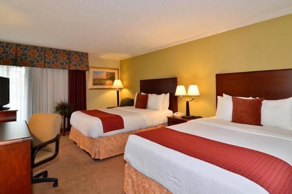 A hotel room with two beds, a desk, a chair, and a television.