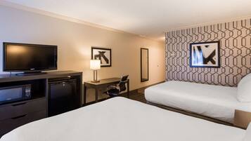 A hotel room with a bed, a desk with a TV, a microwave, and a chair.
