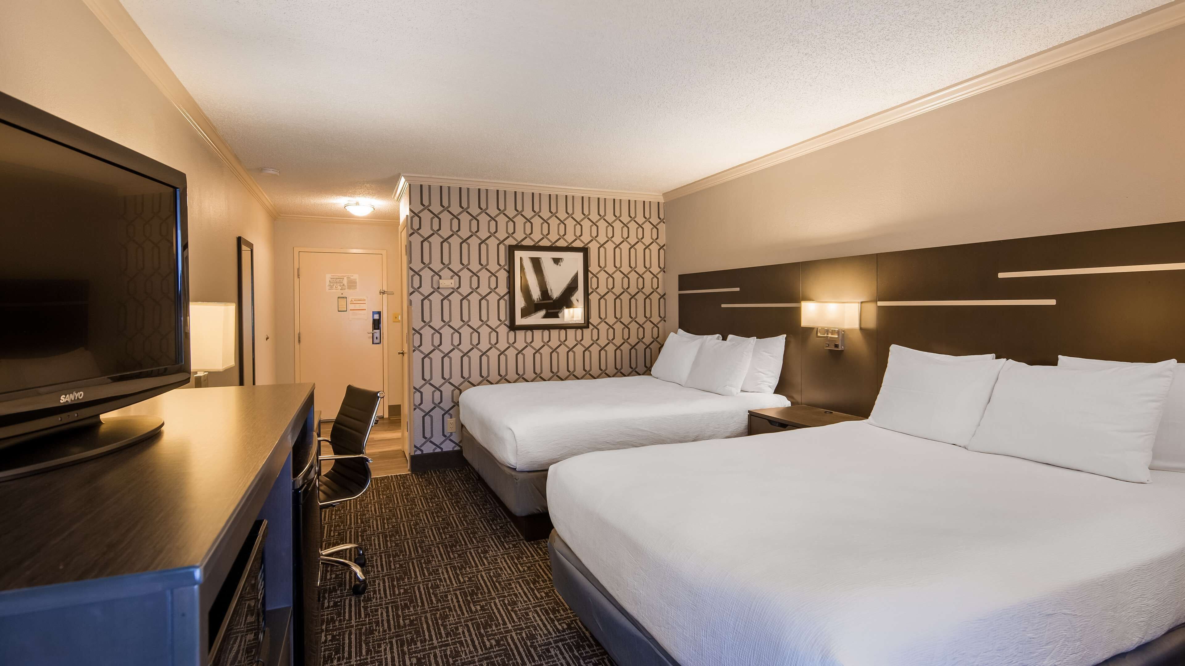 Ein Hotelzimmer mit zwei Betten, einem Schreibtisch mit Fernseher, einem Sessel und einer Wand mit Muster.