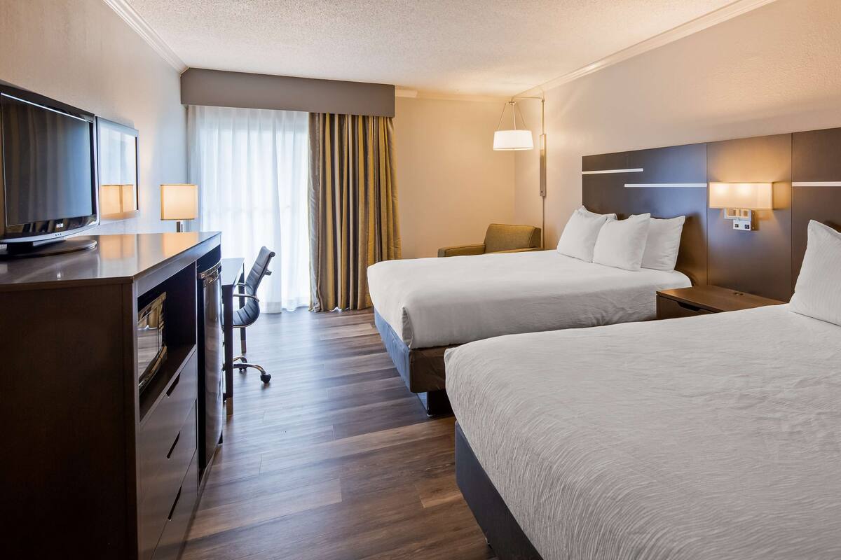 A hotel room with two beds, a desk with a chair, a television, and a window with curtains.