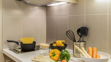 A kitchen with a stove, pots, vegetables, and utensils on the counter.