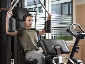 Une personne utilise un appareil de musculation dans une salle de sport, avec une fenêtre donnant sur le paysage en arrière-plan.