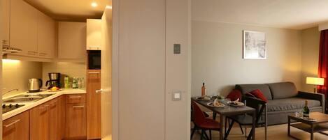 A modern kitchen with wooden cabinets and a dining area with a grey sofa and red chairs.