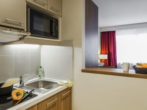 A kitchen with a microwave, sink, and a window with a red curtain.