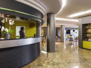 Ett modernt receptionsområde med en böjd receptionsdisk, en receptionist och en orkidé i en kruka.