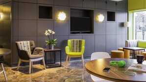 Un salon moderne avec un téléviseur à écran plat, deux fauteuils, une petite table et une plante en pot.