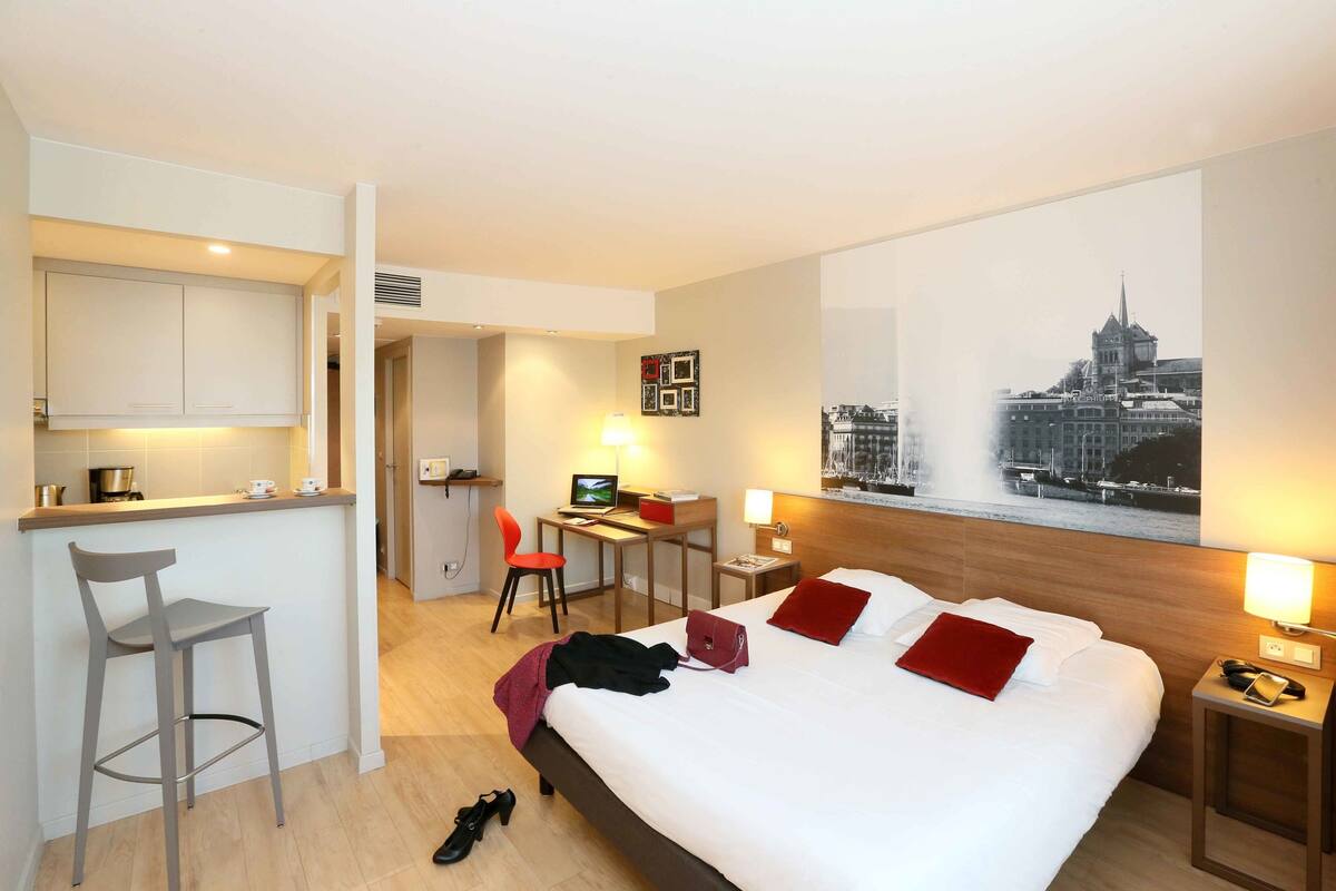 Een hotelkamer met een bed, bureau, stoel en een stadsgezicht schilderij aan de muur.