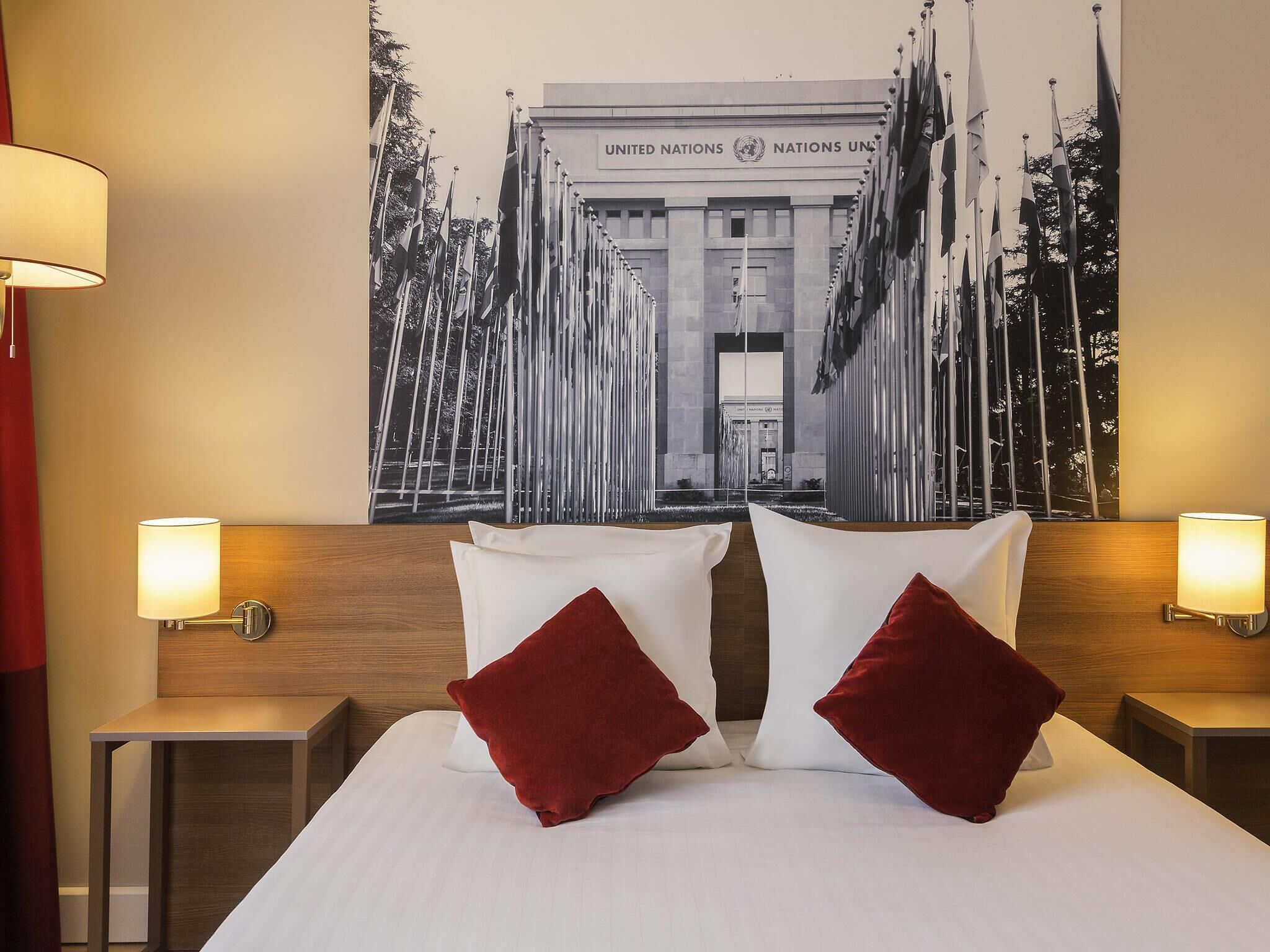 Een hotelkamer met een bed, twee nachtkastjes, twee lampen en een groot poster van het hoofdkwartier van de Verenigde Naties.