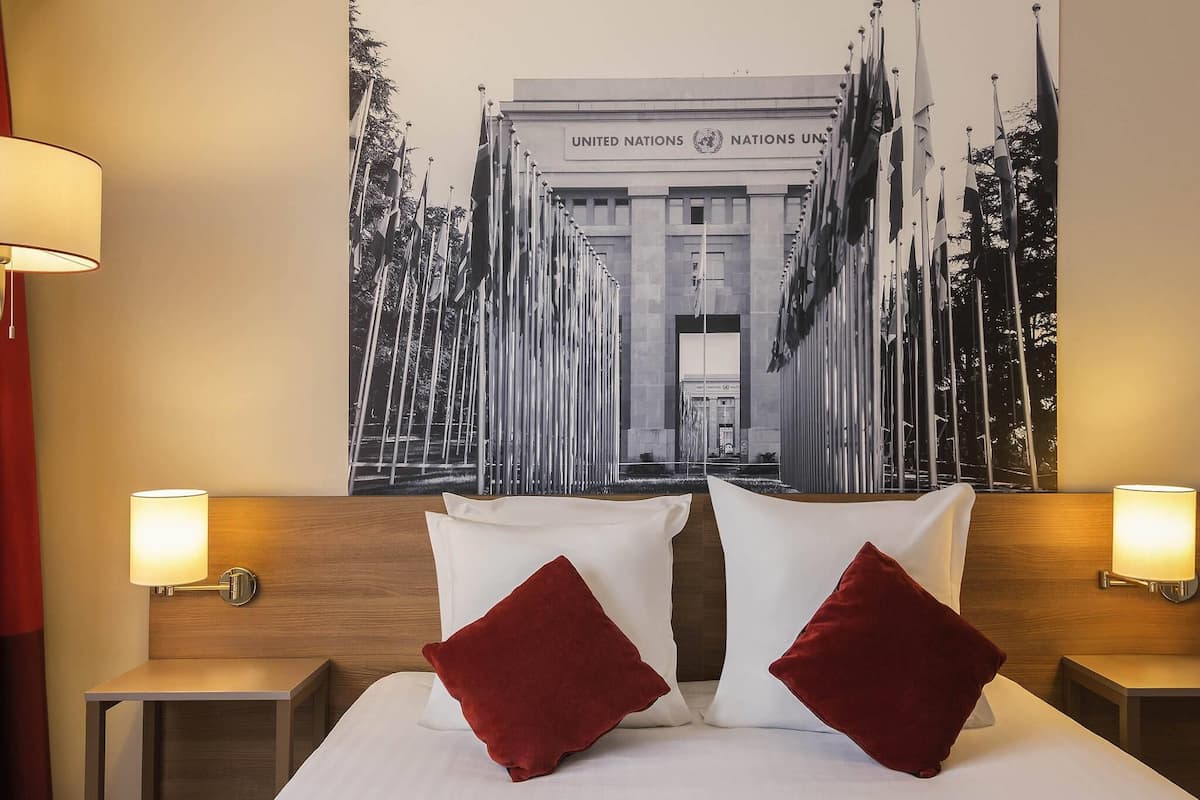 A hotel room with a bed, two nightstands, two lamps, and a large poster of the United Nations building.