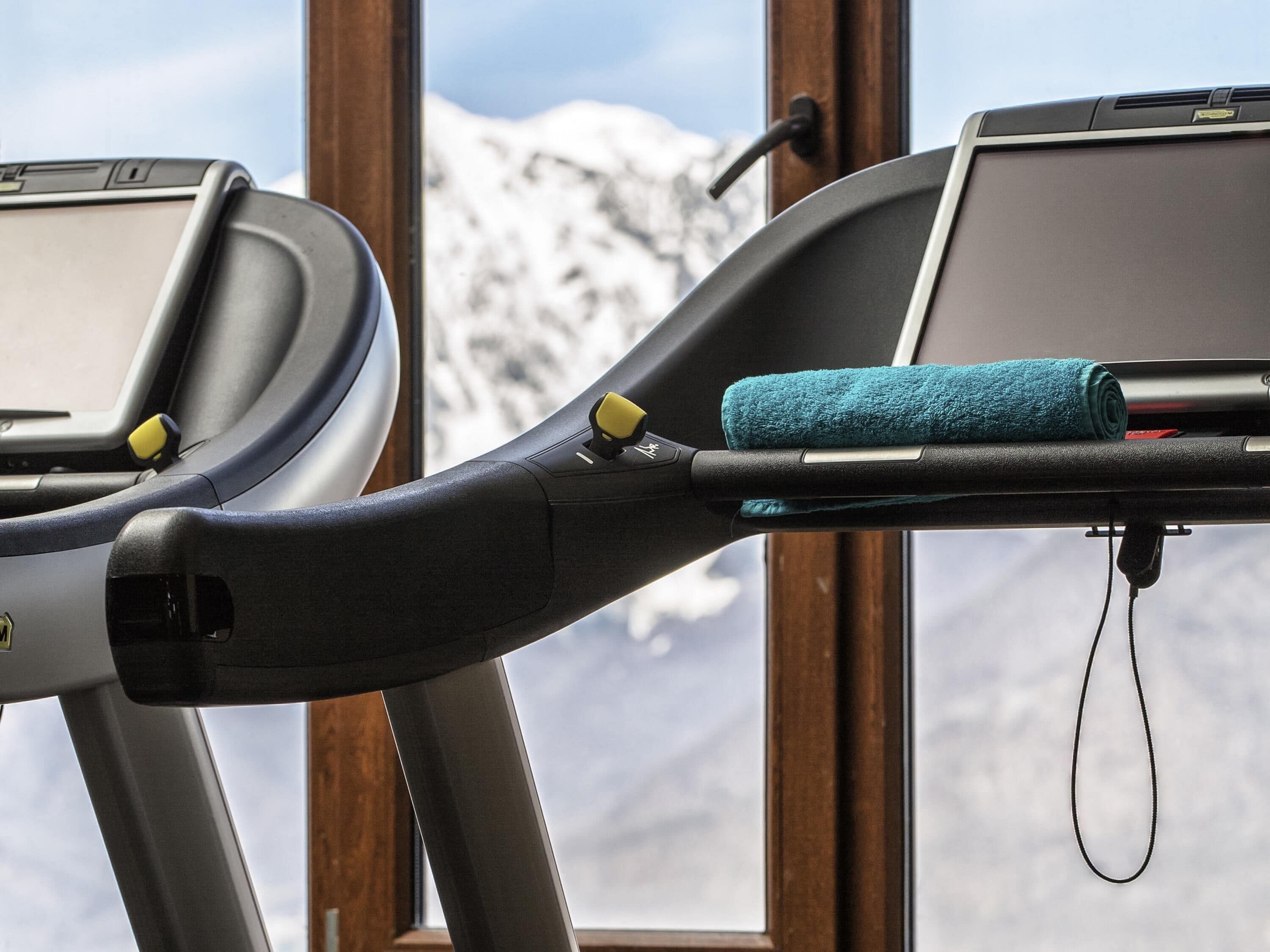 A treadmill with a towel and a charging cable, set against a snowy mountain backdrop.