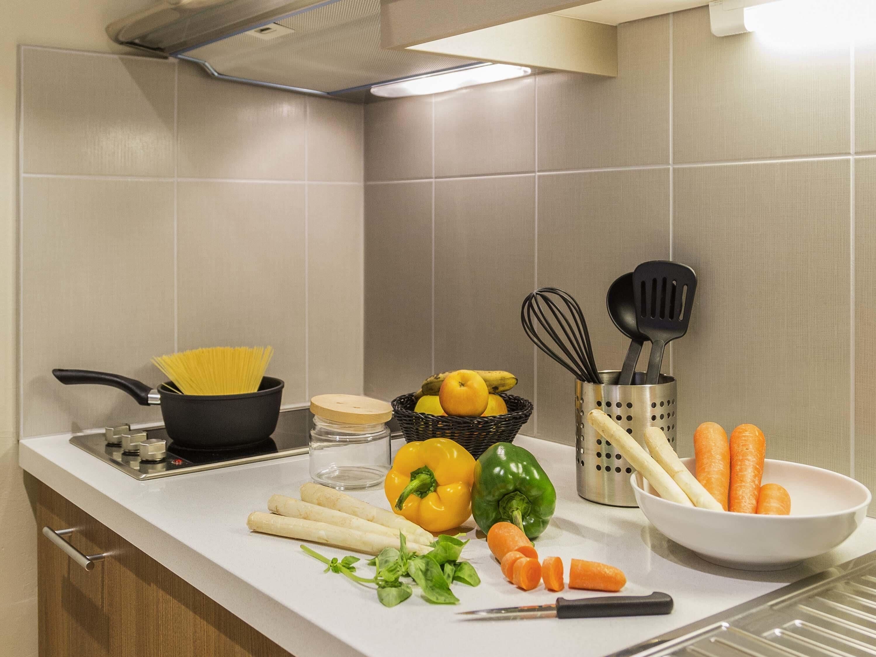 A kitchen counter with cooking utensils, vegetables, and a pan.