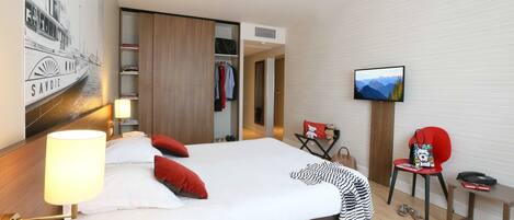 A hotel room with a bed, a TV, a desk, a chair, and a wardrobe.