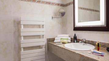Un baño con toallero blanco, lavamanos con artículos de aseo y un espejo.