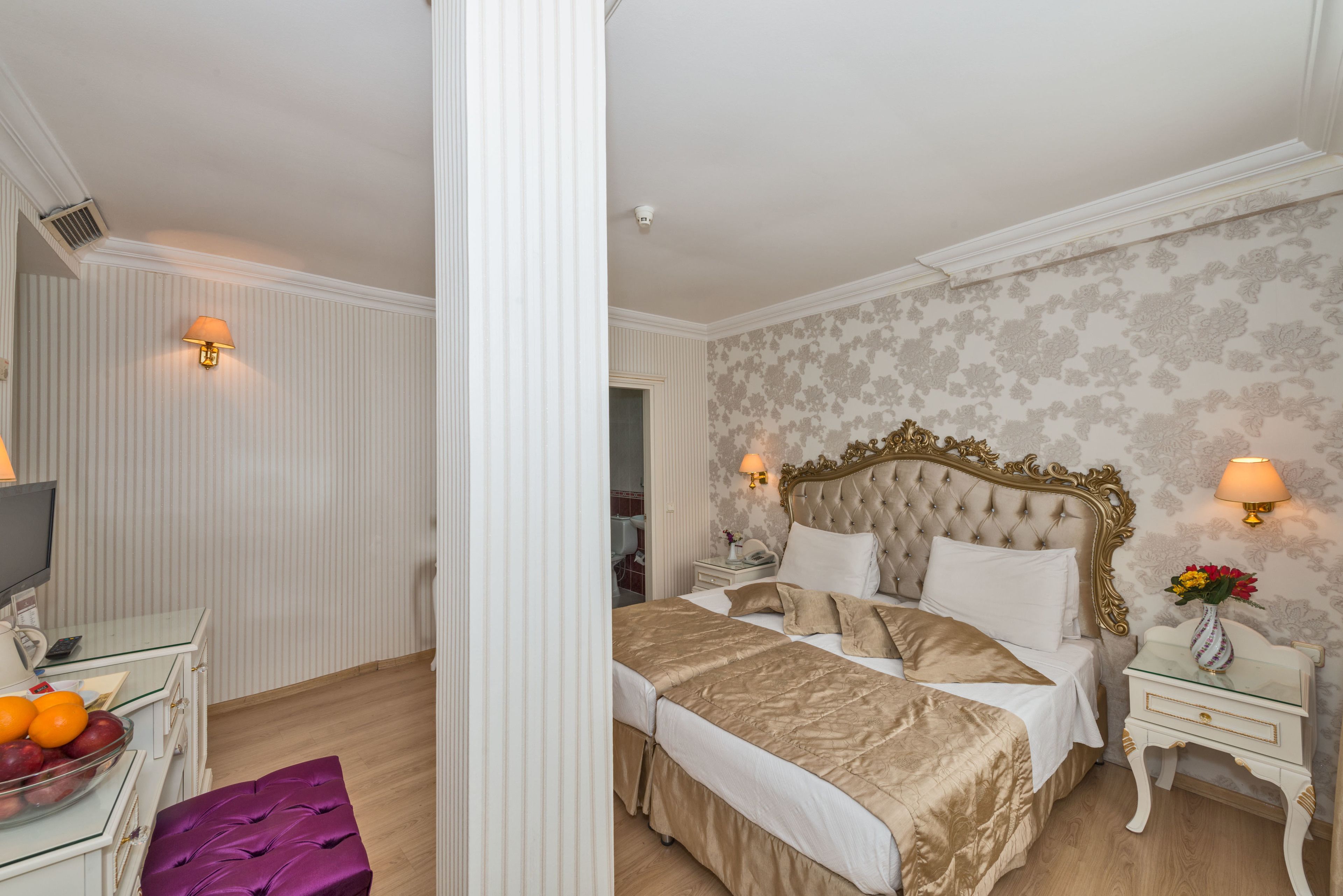 Une chambre à coucher avec un grand lit, des tables de chevet, une télévision et un panier de fruits.