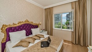 Ein Hotelzimmer mit einem großen Bett, einem Laptop auf dem Bett, einem Nachttisch mit Lampe und einem Fenster mit Vorhängen.