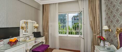 Quarto de hotel com cama, escrivaninha com computador, televisão e janela com cortinas.