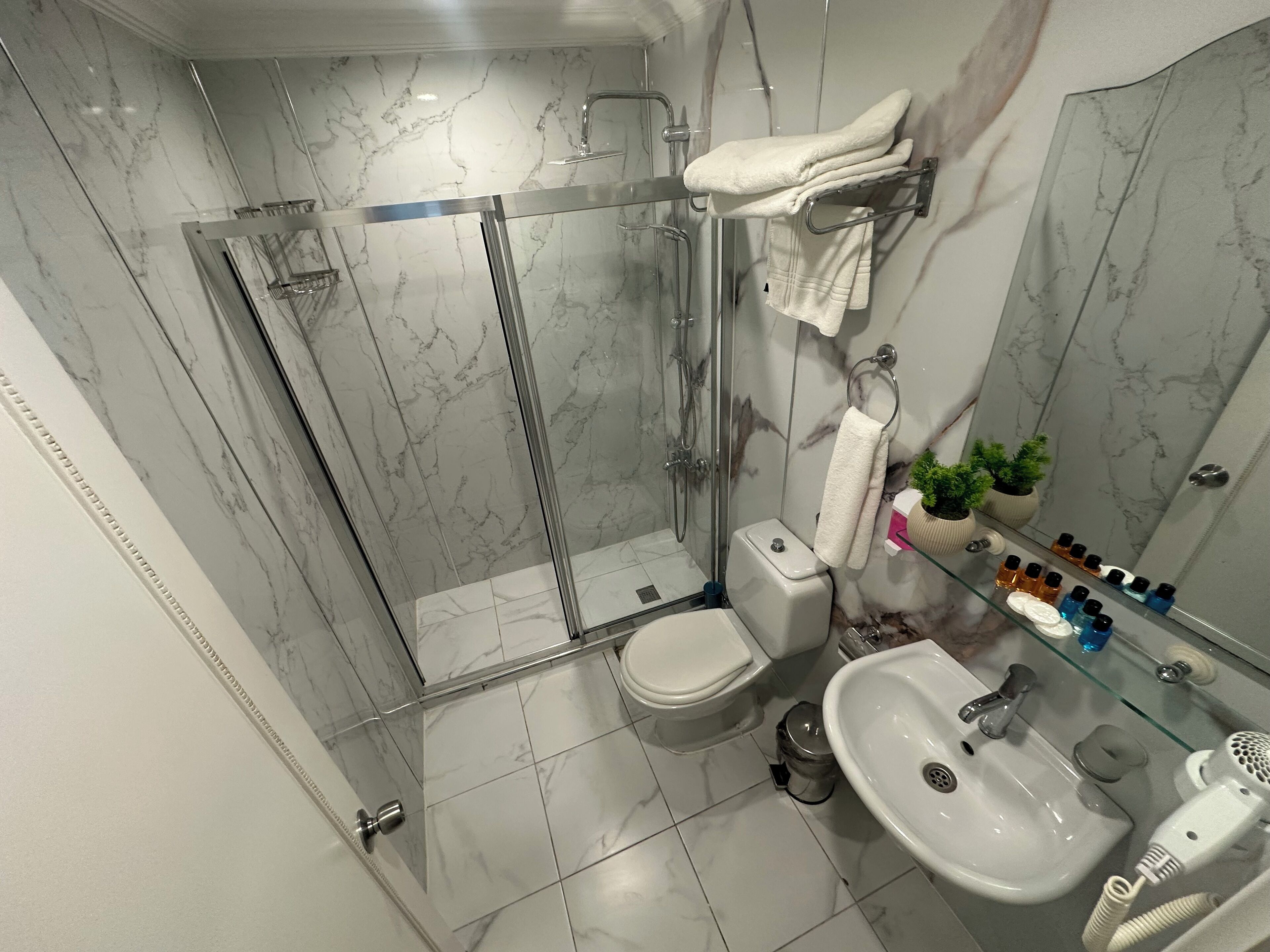 Une salle de bain moderne avec une douche en verre, des toilettes, un lavabo et un miroir agrémenté d’accessoires de toilette.