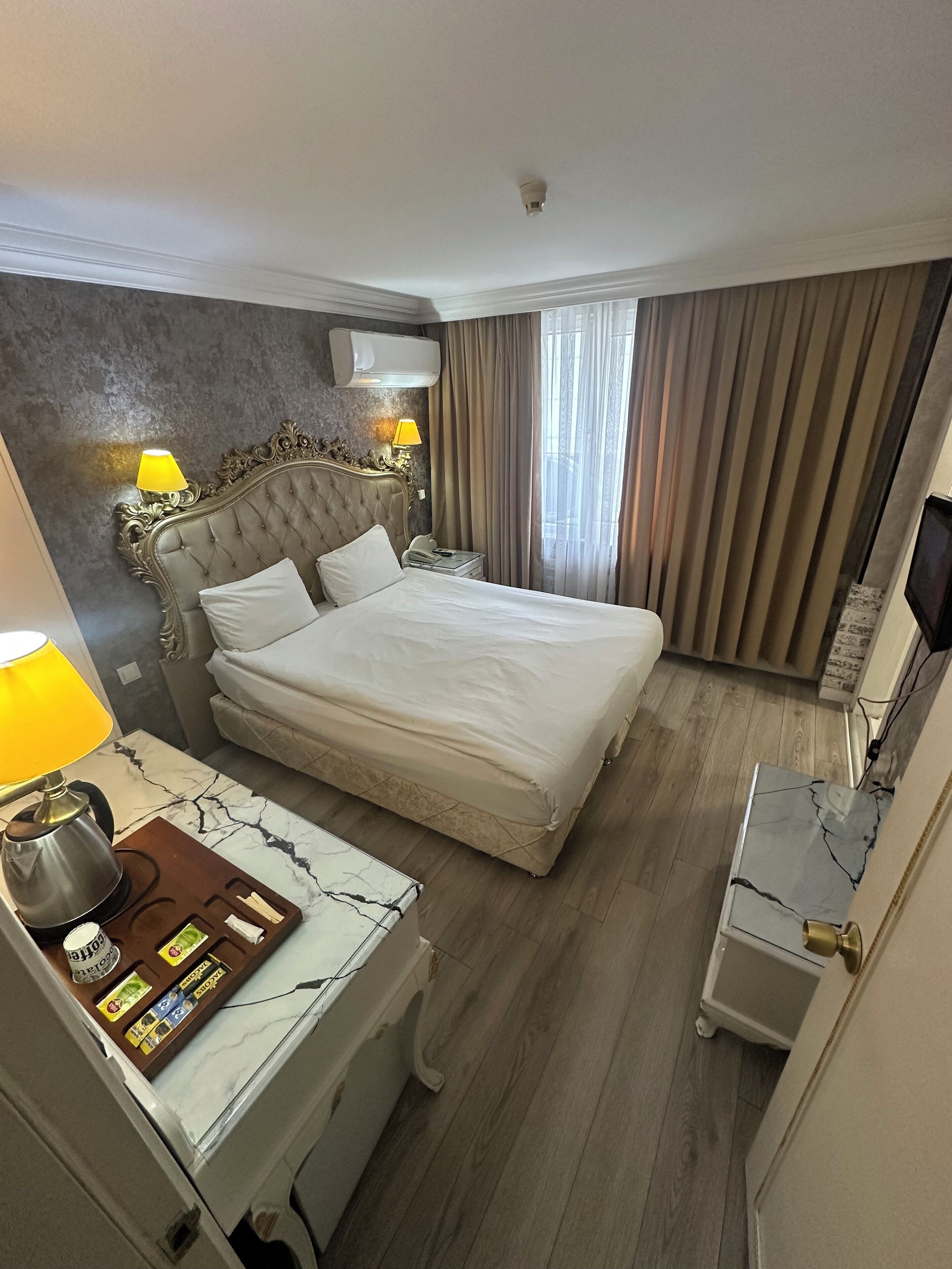A hotel room with a large bed, a bedside table with a lamp, a TV, and a minibar.