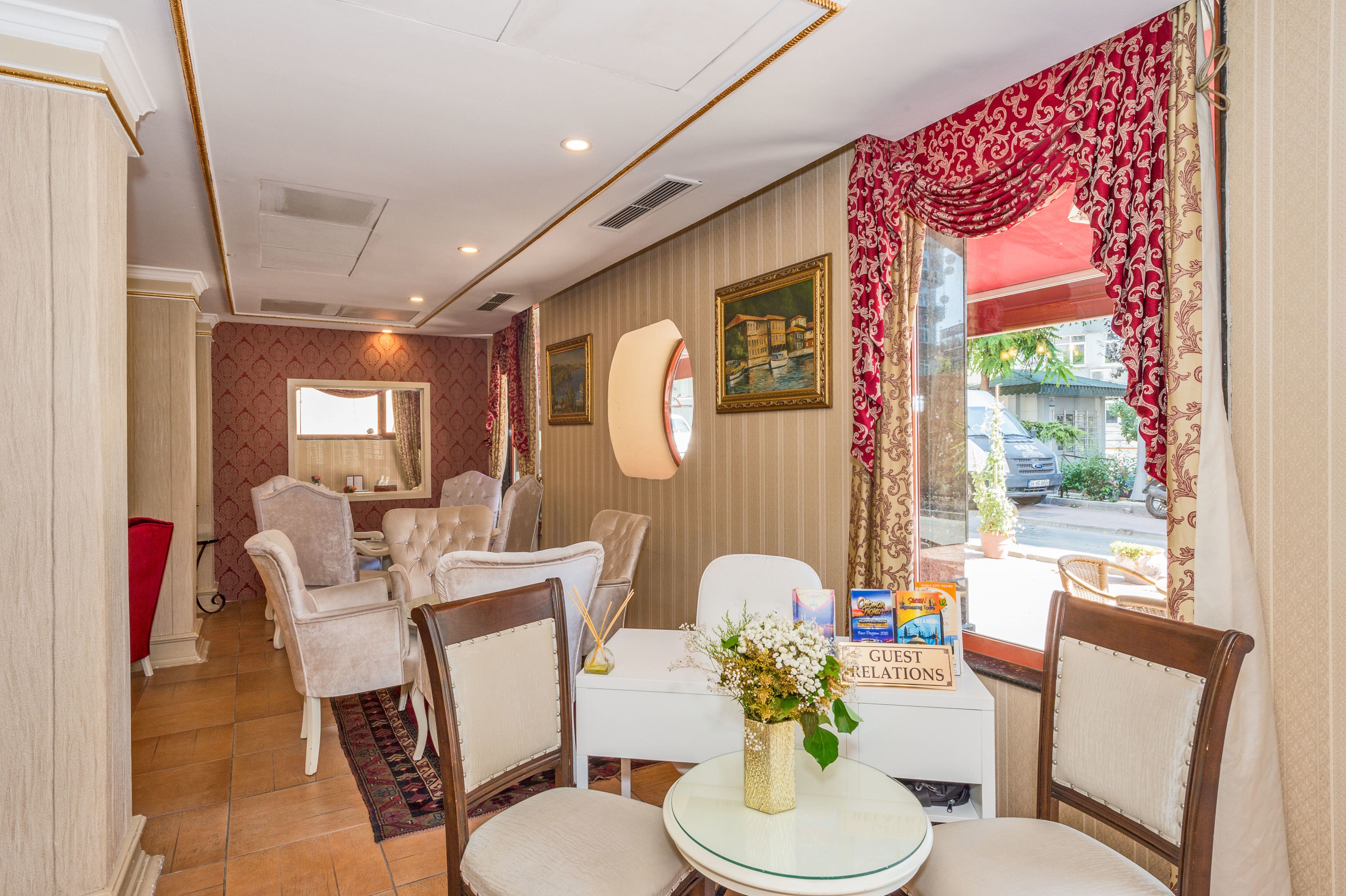 A hotel room with a dining area, a desk with a vase of flowers, and a view of the street.