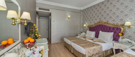 A hotel room with two beds, a vanity with a mirror, and a small table with a tray of fruit and tea.