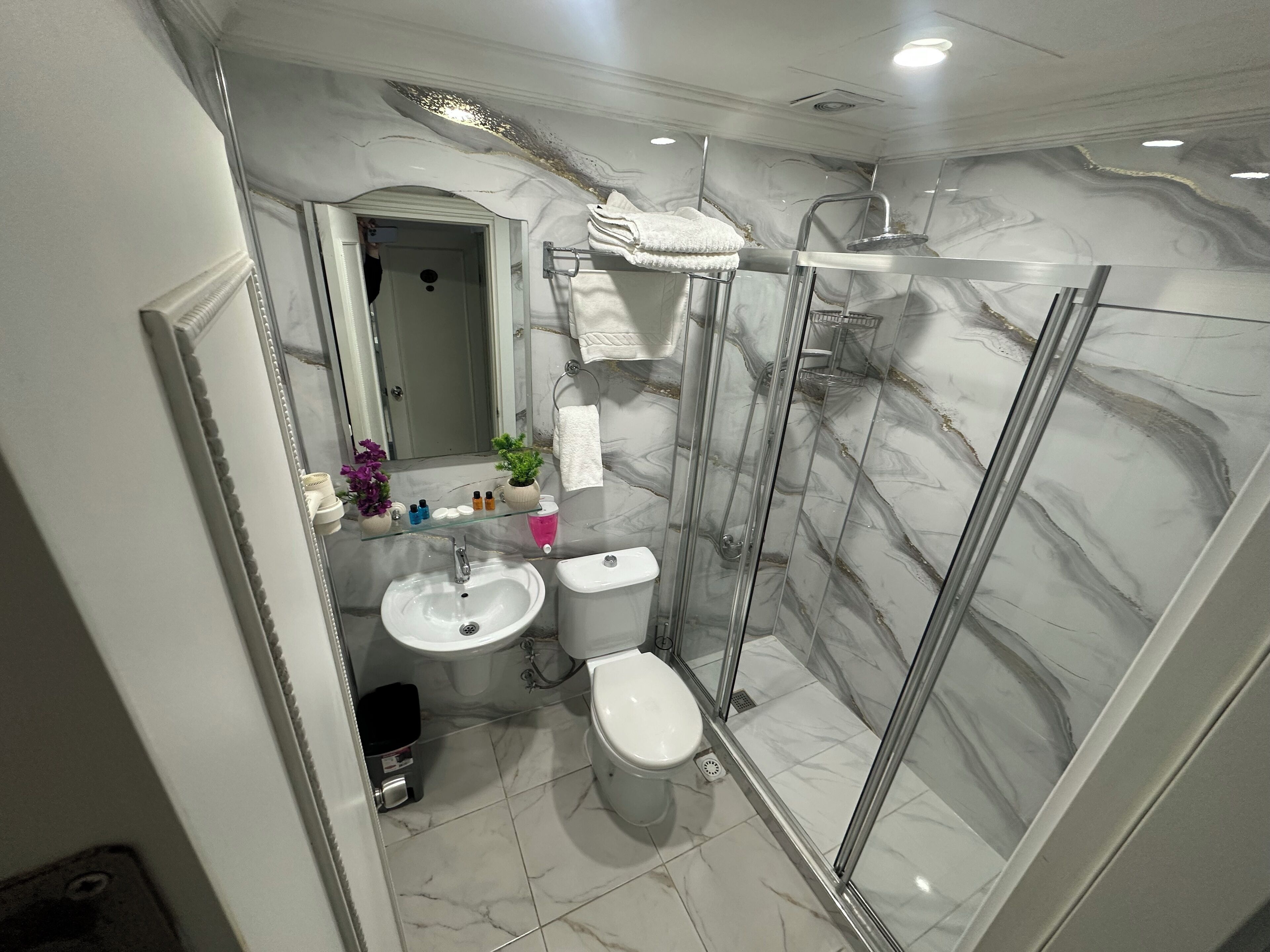 A bathroom with a marble floor, a glass shower enclosure, a toilet, and a sink with a mirror above it.
