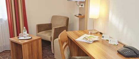 A hotel room with a wooden desk, two chairs, a television, a lamp, and a telephone.