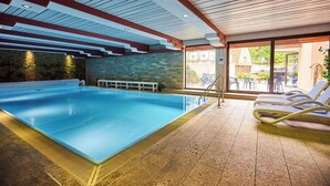 Una piscina interior con un banco, sillones de descanso y una pared de piedra.
