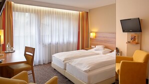 Habitación de hotel con cama, dos mesitas de noche, televisor, escritorio con silla y ventana con cortinas.