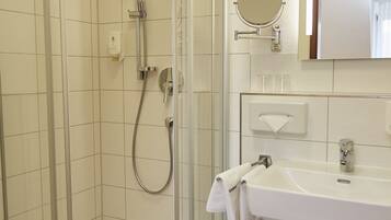 A modern bathroom with a glass-enclosed shower, a white sink, and a mirror above it.