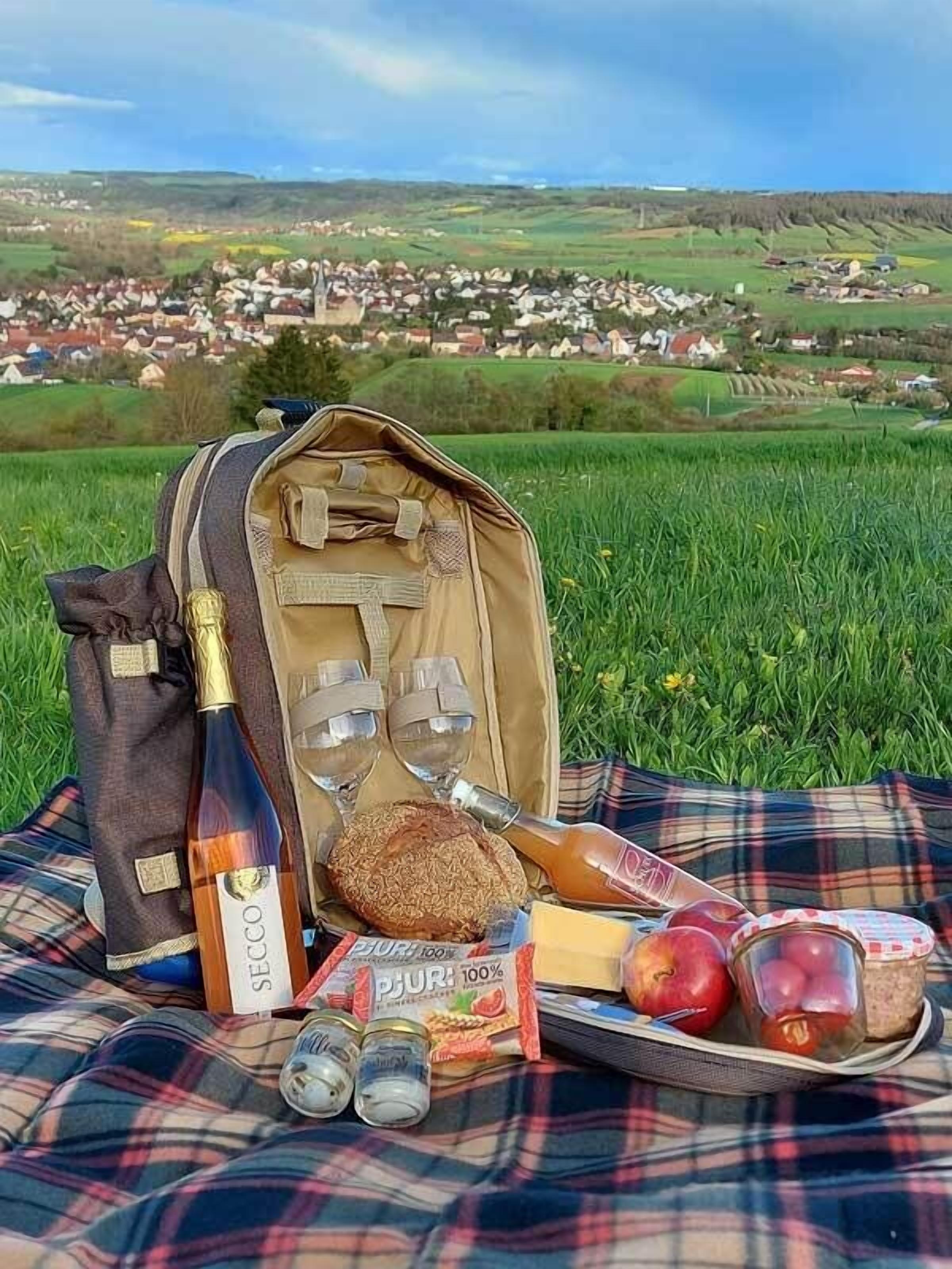 Un montaje para picnic con una botella, vasos, pan, manzanas y condimentos sobre una manta.