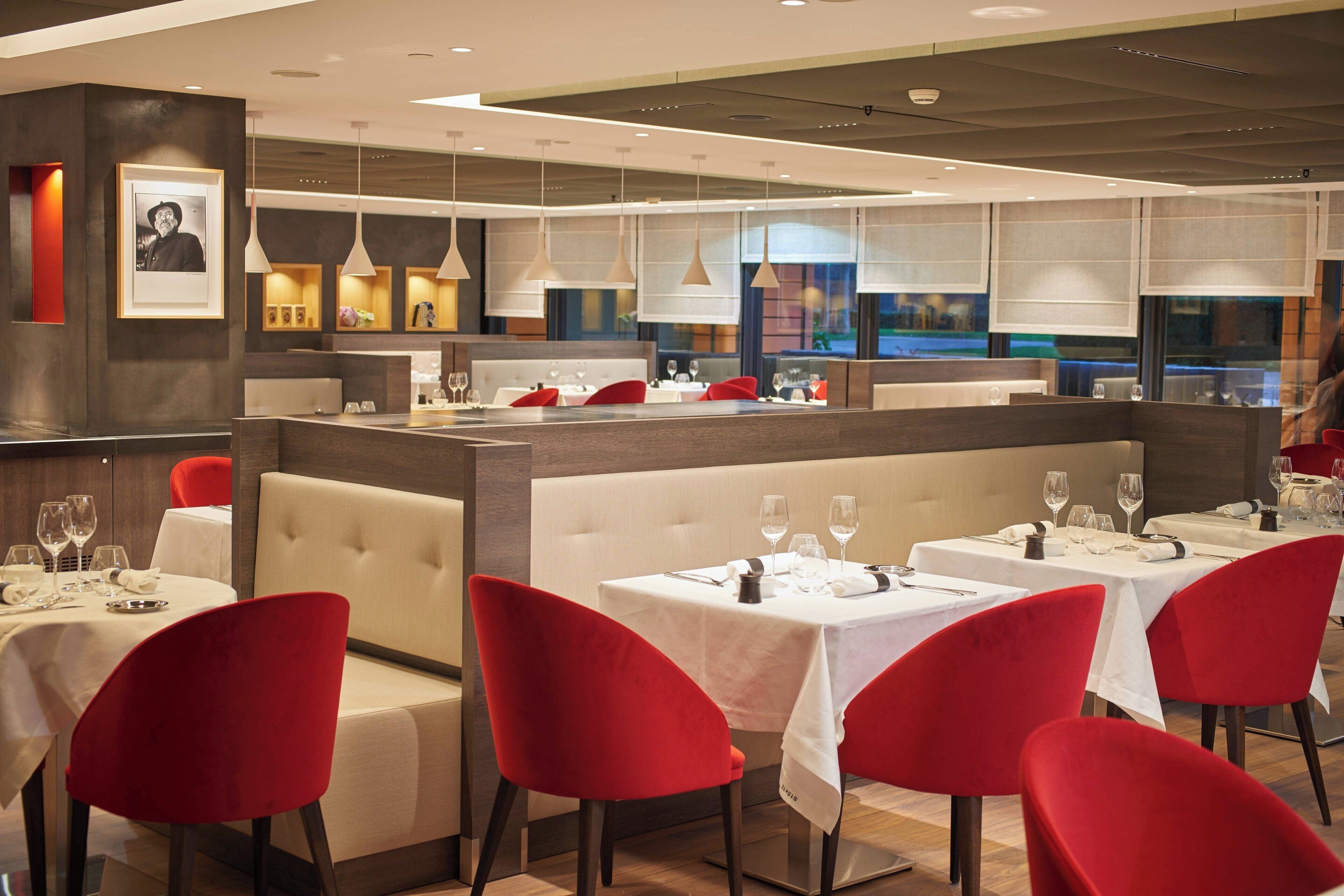 A restaurant with multiple tables, red chairs, and a bar area.