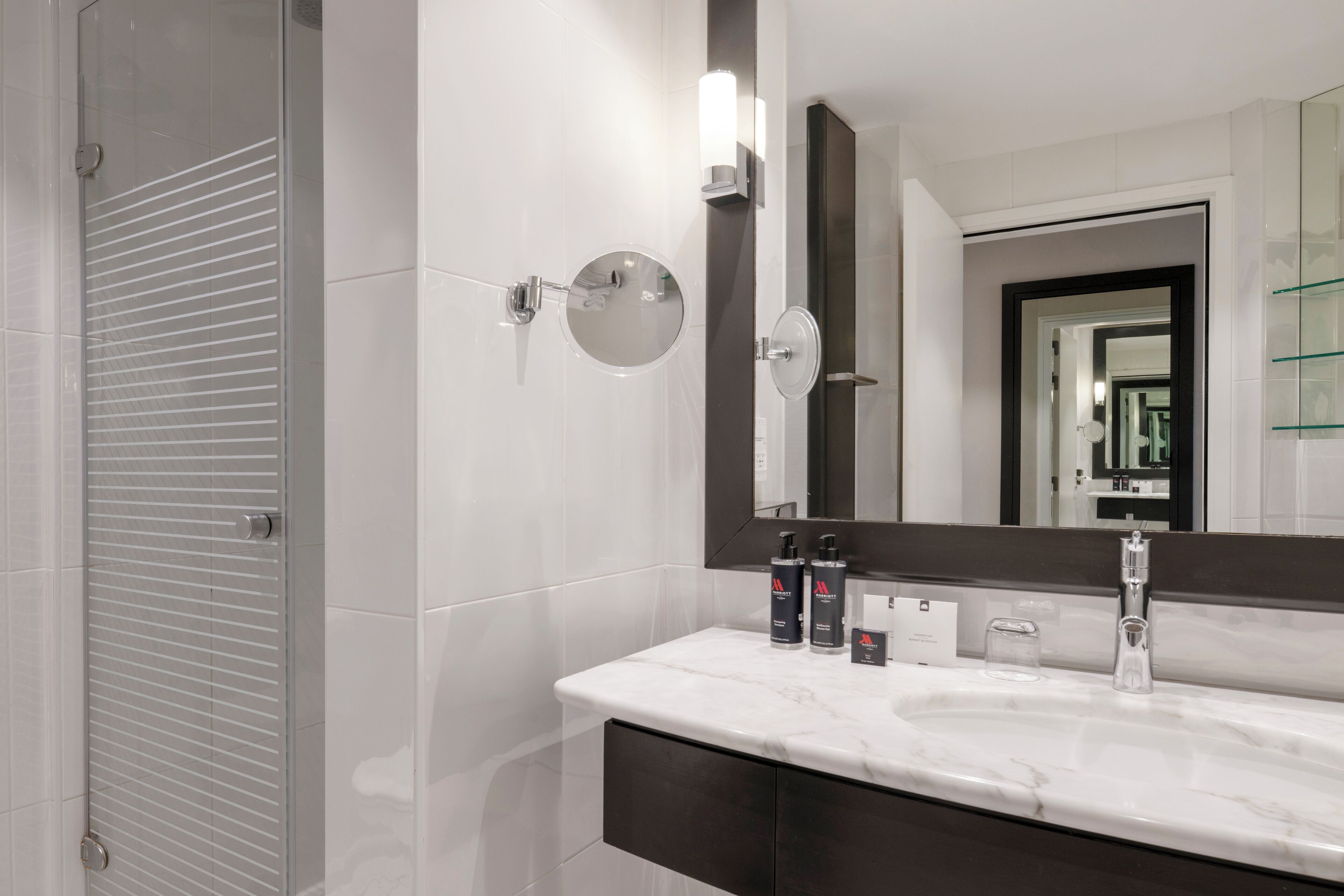 A modern bathroom with a large mirror, a sink with a marble countertop, and a shower with a glass door.