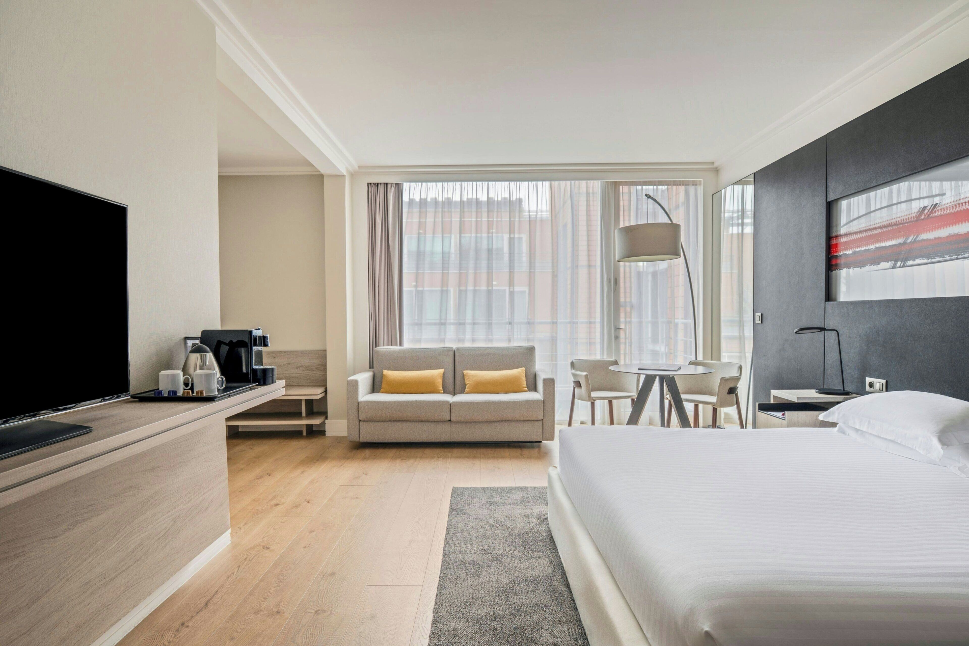 A hotel room with a bed, a sofa, a desk, a chair, a TV, and a coffee maker.