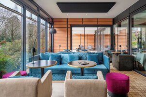Un'area lounge moderna con un divano blu, tavolini rotondi e vista sull'esterno.