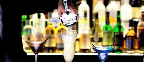 A bar with three cocktails, a bartender's hand, and a variety of bottles in the background.