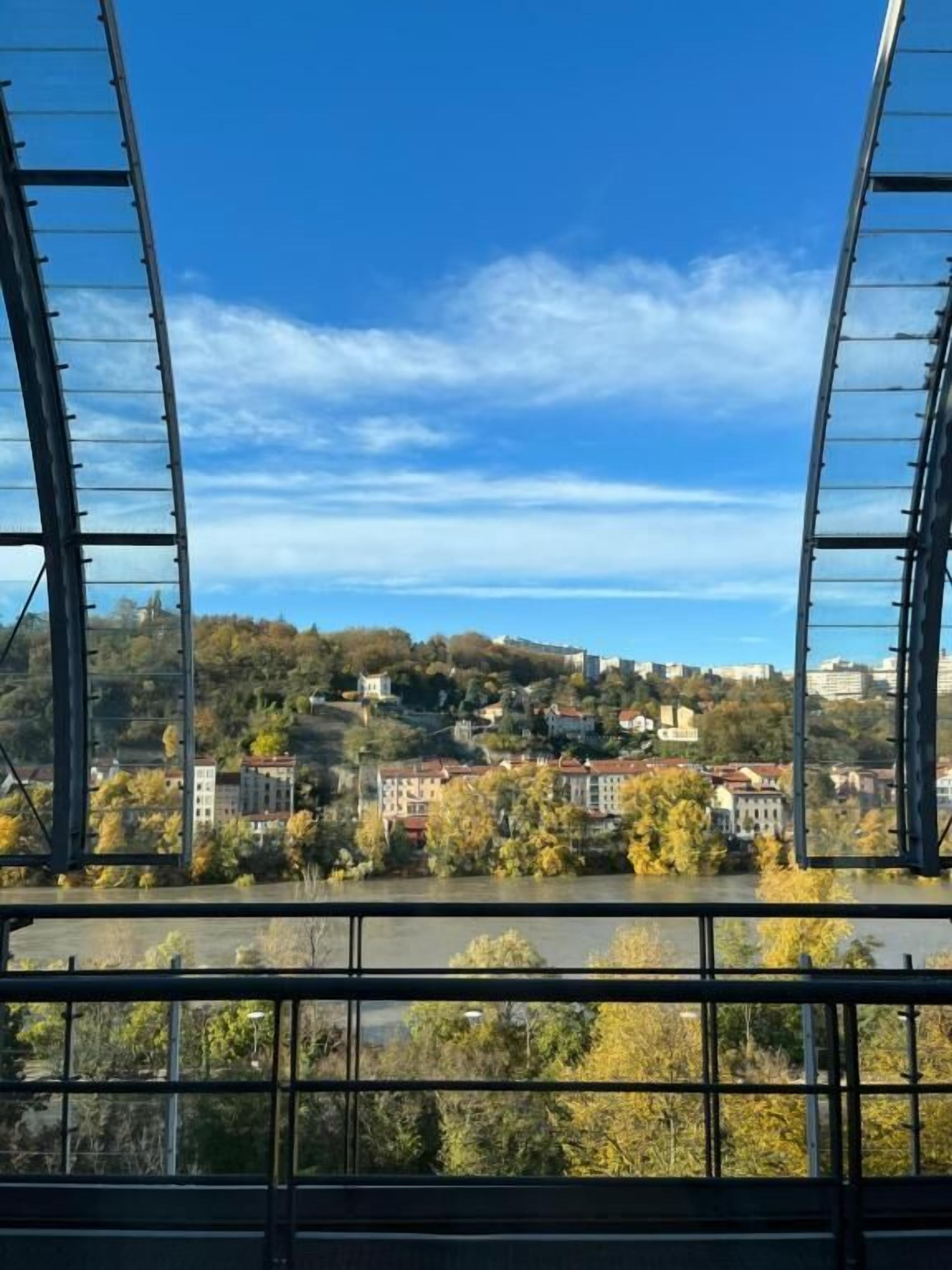 Uitzicht vanaf een brug met een metalen hekwerk, uitkijkend over een stad met gebouwen en bomen.