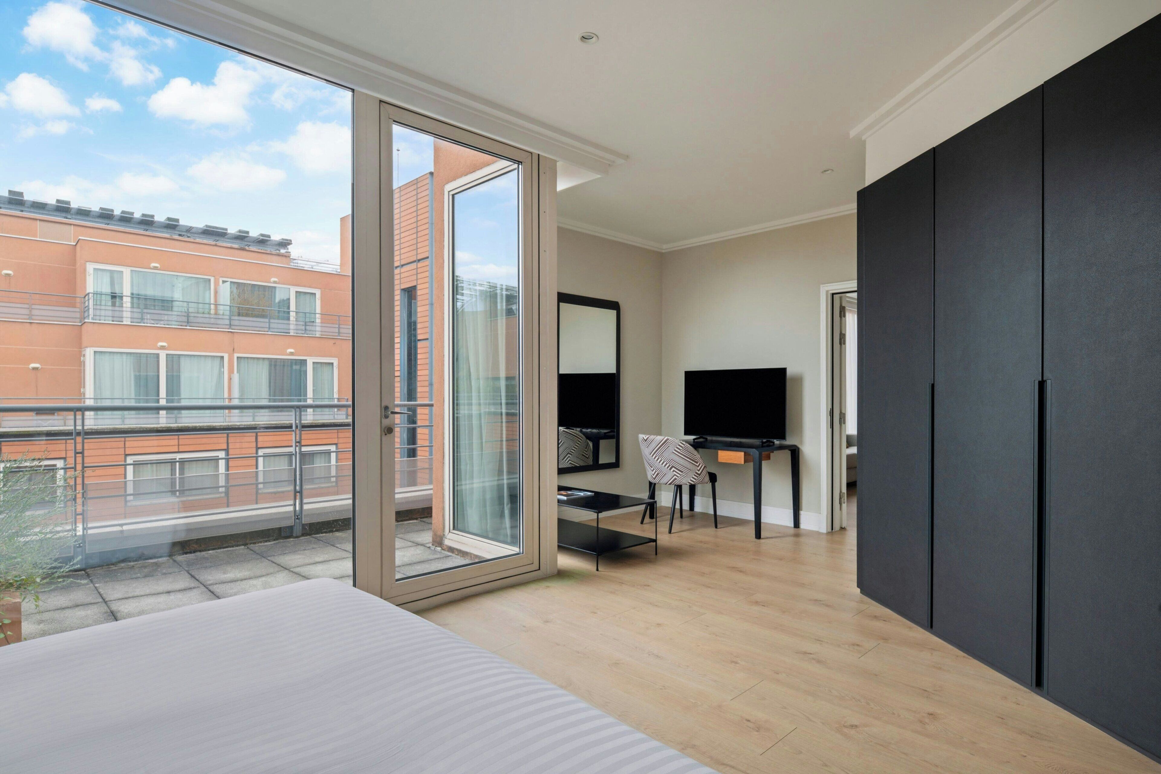 Une chambre moderne avec un grand lit, un bureau avec une chaise, une télévision et une porte-fenêtre coulissante donnant sur un balcon.