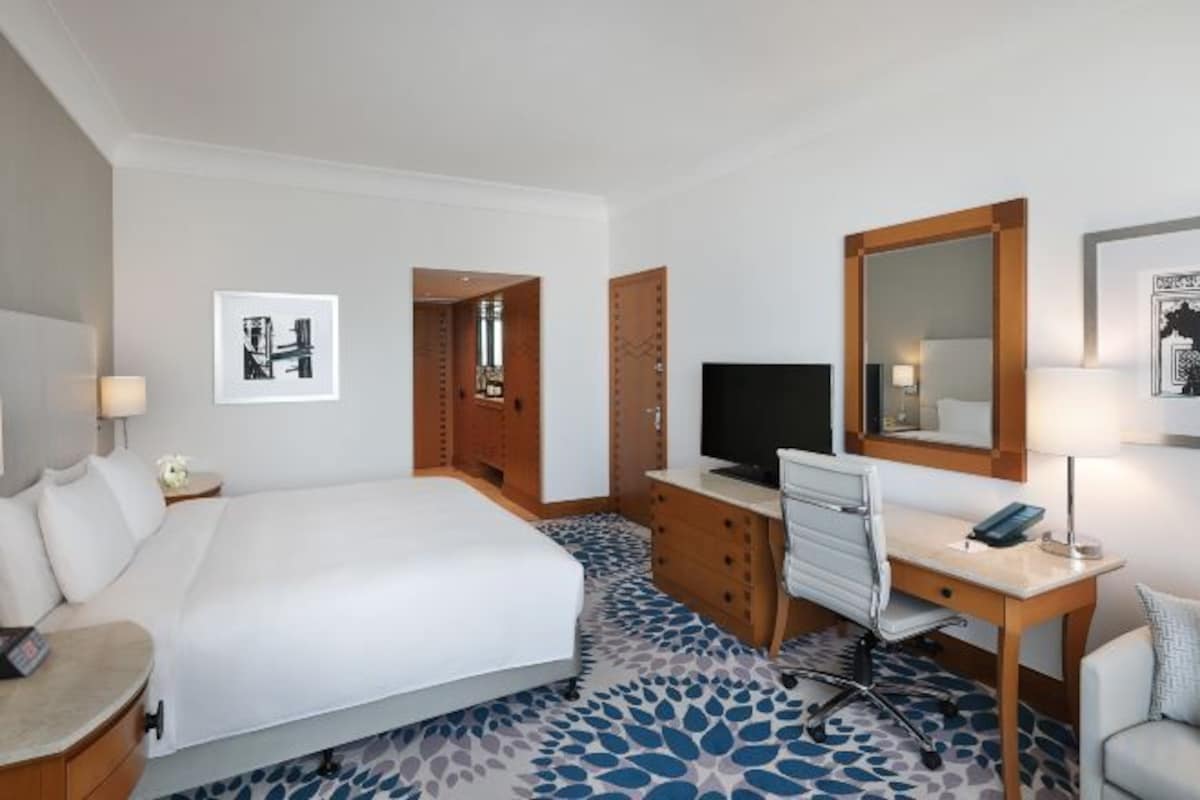 A hotel room with a large bed, a desk, a television, and a mirror.