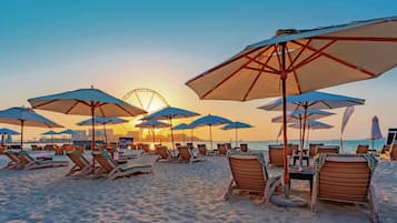 A beach with sun loungers and umbrellas, a Ferris wheel in the background, and a clear sky.