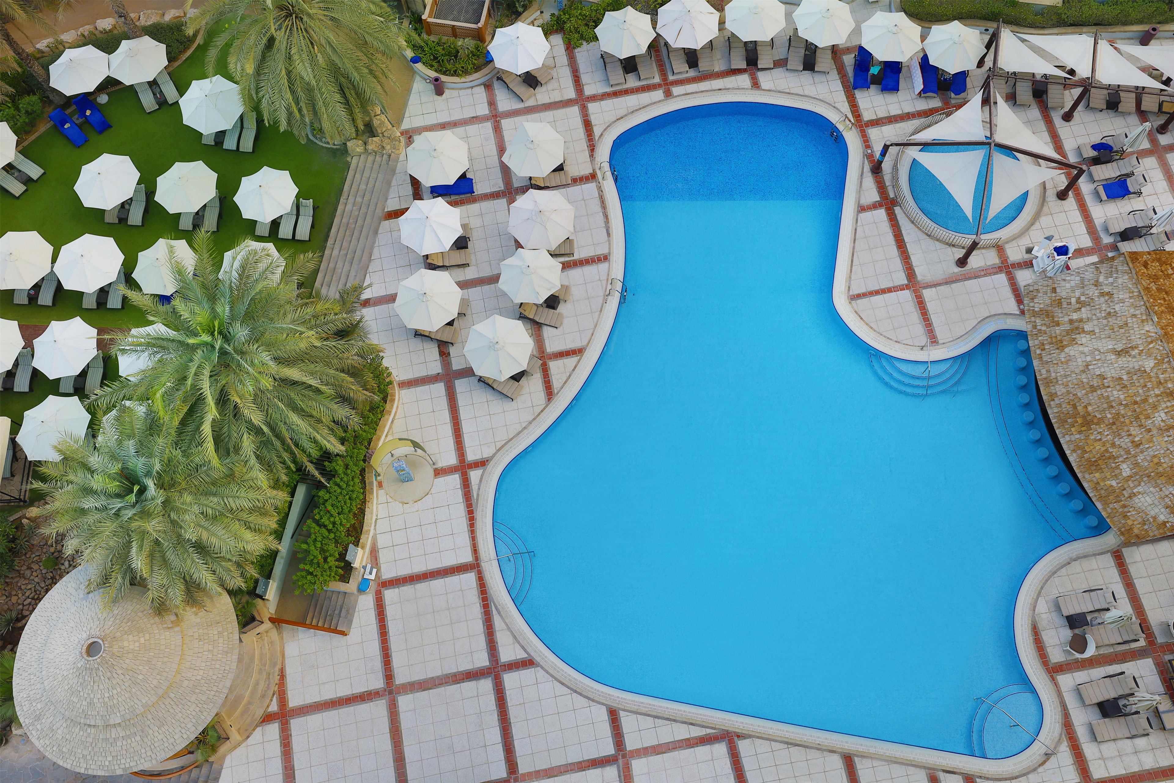 Ein Pool mit ungewöhnlicher Form, umgeben von Liegestühlen und Sonnenschirmen.