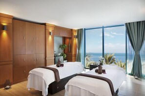 A hotel room with two beds, a large window with a view of the sea, wooden furniture, and a small table with a plant. - Hilton Dubai Jumeirah (Dubai)