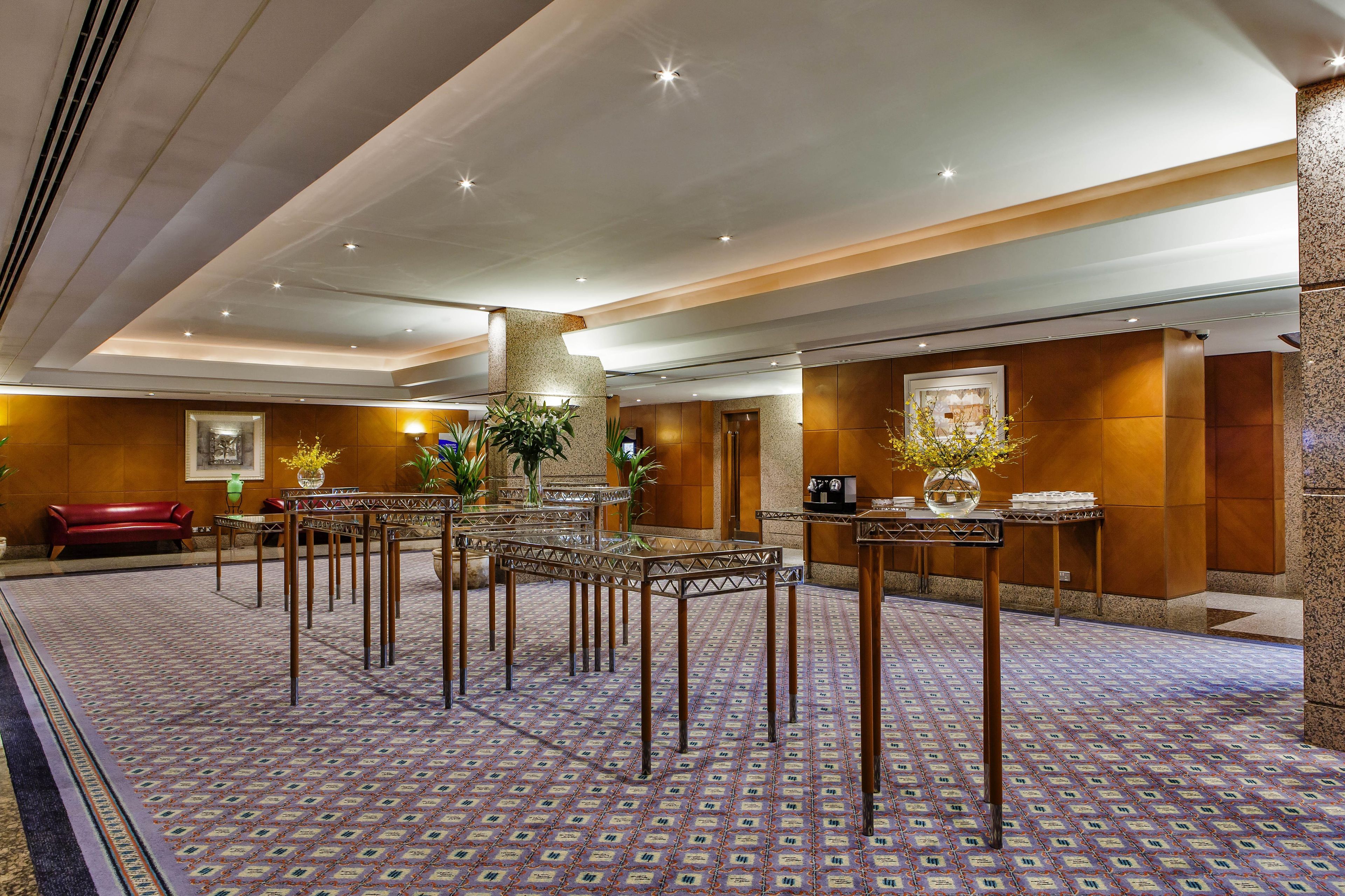A hotel lobby with a patterned carpet, multiple tables, a red sofa, and decorative plants.