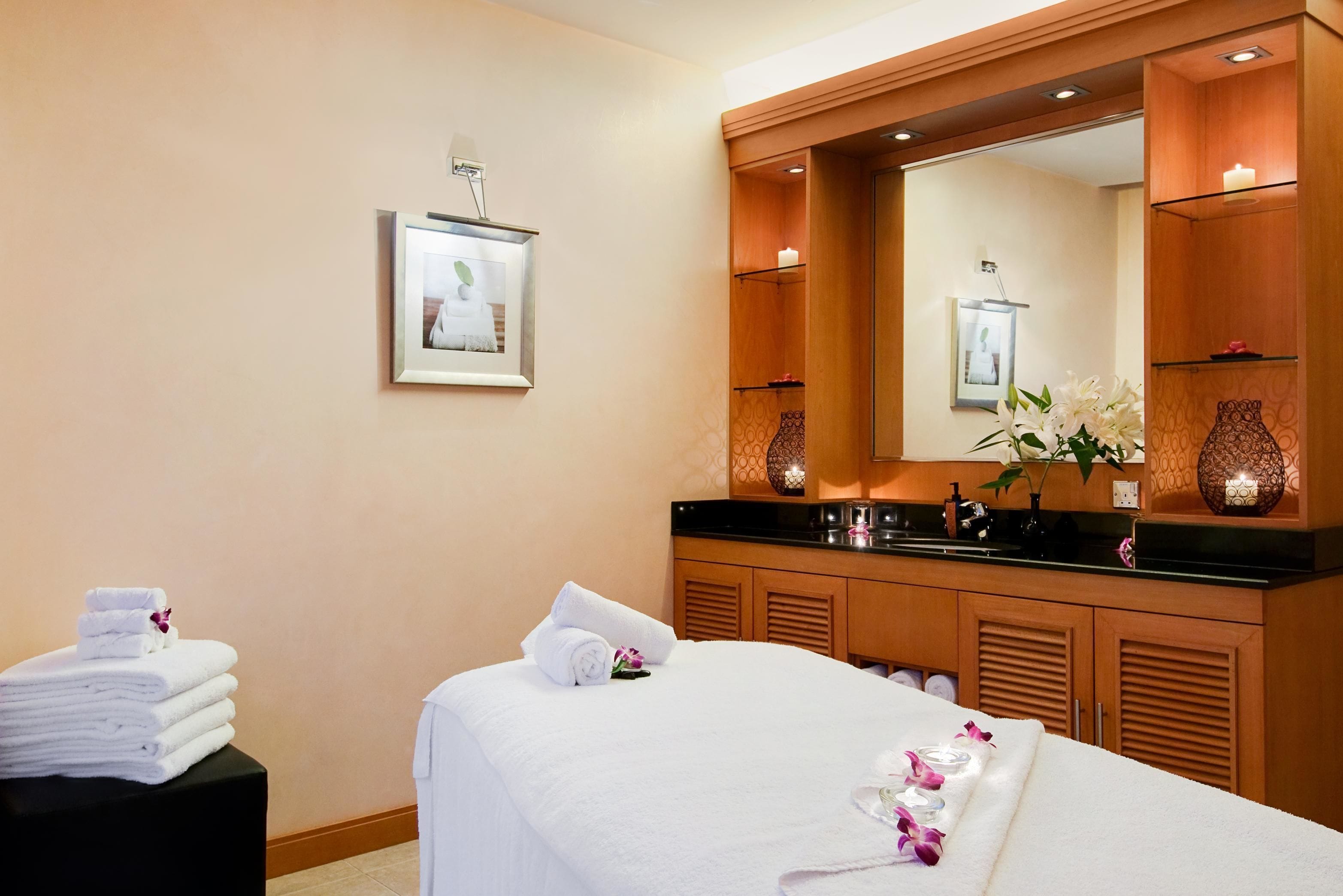 A hotel room with a bed, a large mirror, a vanity with a sink, and a framed picture on the wall.
