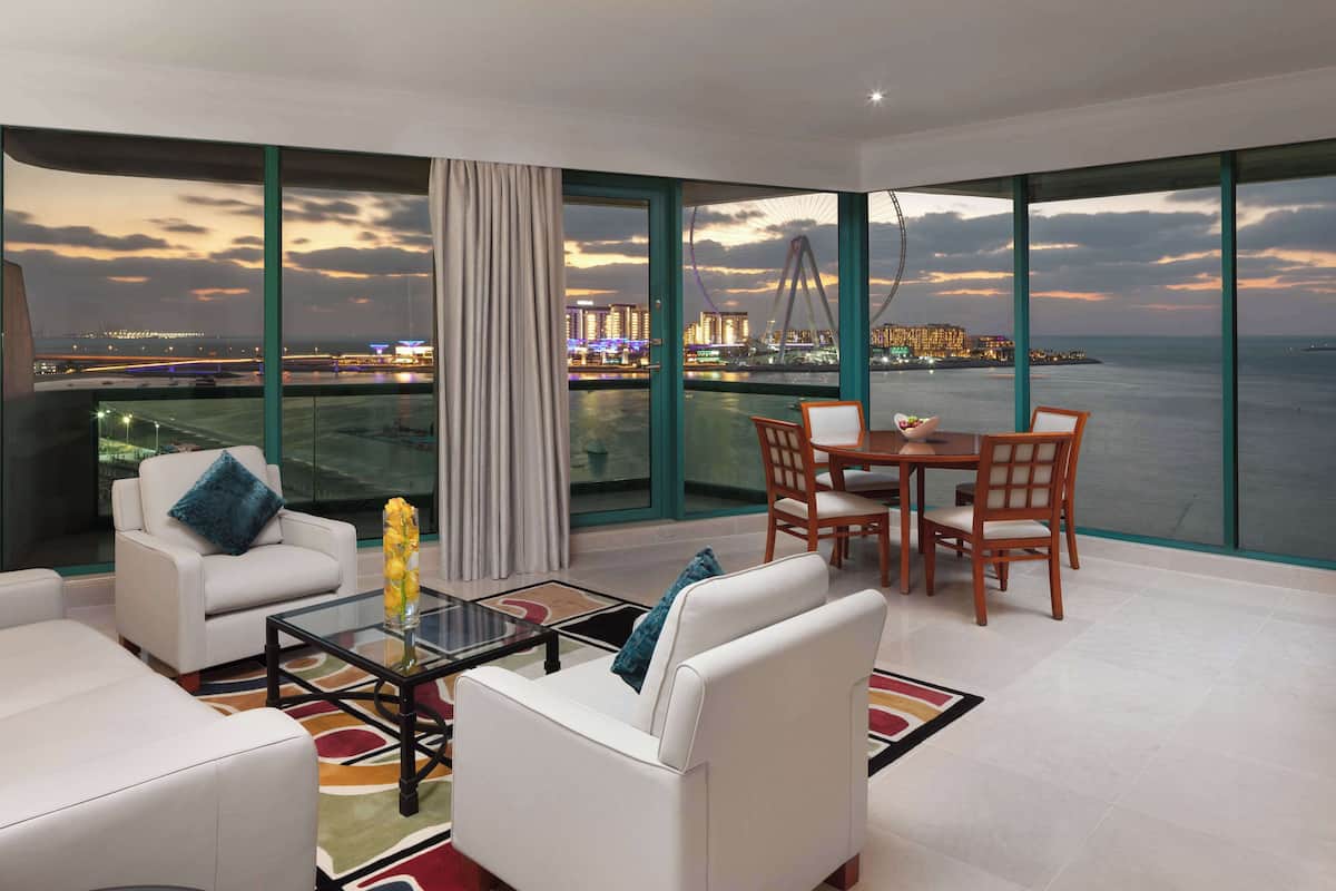 A modern living room with a city view, large windows, and a dining area with a table and chairs.