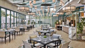 A spacious indoor dining area with multiple tables and chairs, large windows, and a modern ceiling design. - Hilton Dubai Jumeirah (Dubai)