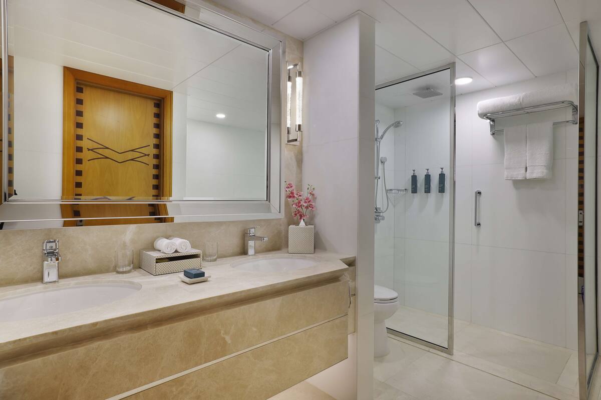 A modern bathroom with a large mirror, a sink, a glass shower enclosure, and a toilet.